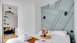 A hotel room with a bed, a wooden side table, a vase with flowers, and a wall with geometric patterns. - Beautiful Cozy Apartment - 1 Bdr/4p - Gare de Lyon / AC (Paris)