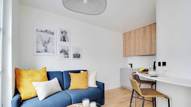 A modern living room with a blue sofa, a wooden dining table, and a kitchen area with wooden cabinets. - Beautiful Cozy Apartment - 1 Bdr/4p - Gare de Lyon / AC (Paris)