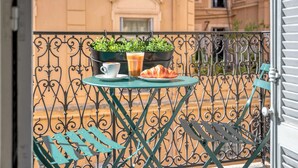 Un balcón con una mesa lista para dos personas, que incluye una taza, un vaso de café helado y un croissant.