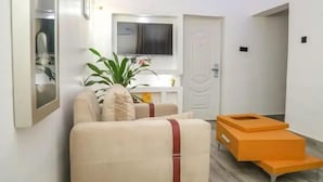 Een moderne woonkamer met een bank, een aan de muur bevestigde televisie en een plant.