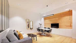 A modern living room with a grey sofa, a dining table with chairs, a TV mounted on a wooden wall, and recessed ceiling lights. - Haven of Peace-2br/4p- Opera Garnier / Madeleine (Paris)