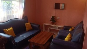 Een woonkamer met twee donkerblauwe banken, elk met een geel kussen, een houten salontafel en een klein witte bijzettafel met een plantje.