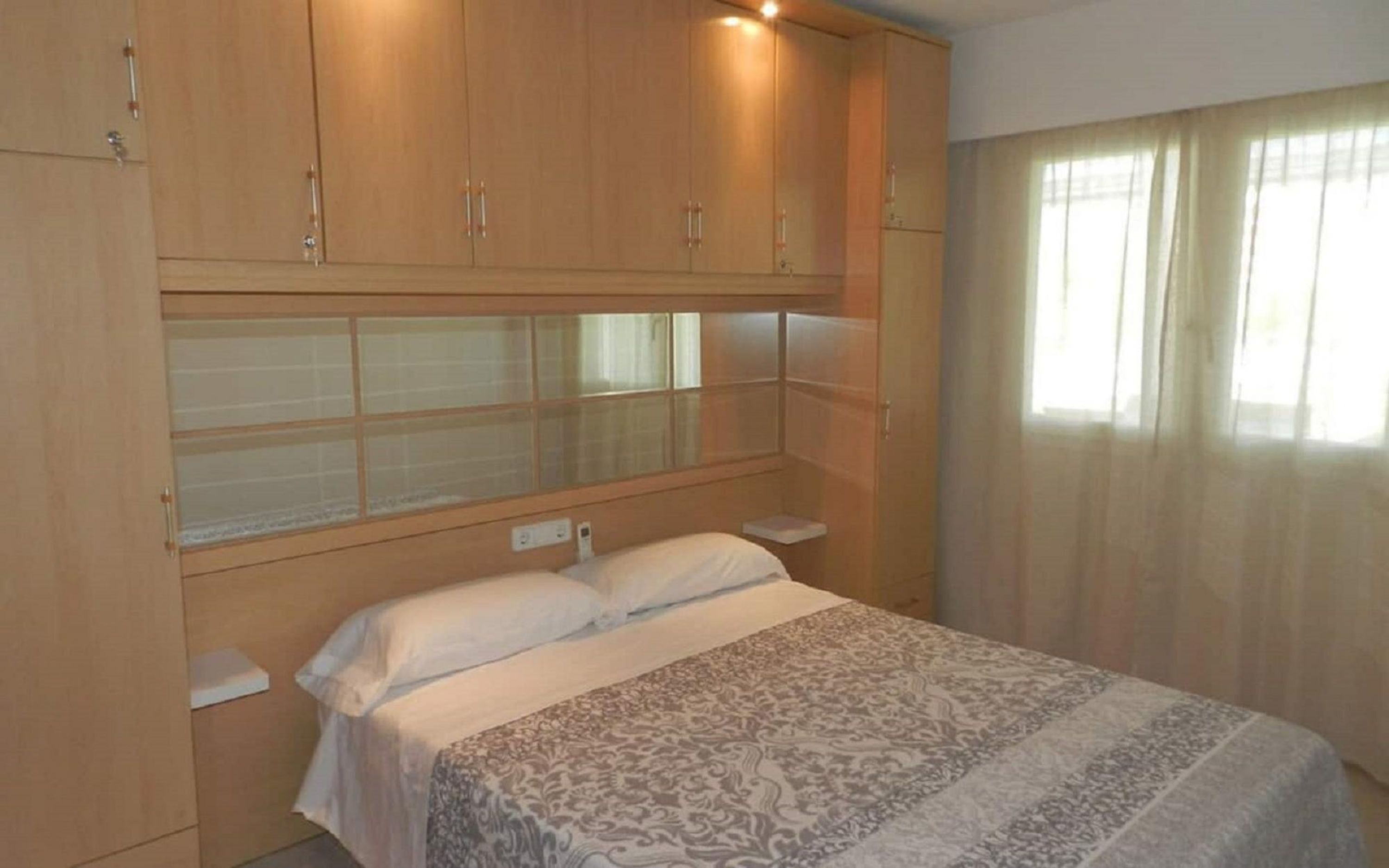 A bedroom with a bed, wooden cabinets, and a window with curtains.