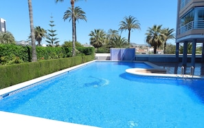 A clear blue swimming pool with a geometric tile pattern, surrounded by palm trees and a hedge. - Apartamento Talima Para 6 Personas (Calpe)