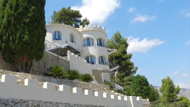 A white, multi-story building with arched windows and balconies, surrounded by greenery and a stone wall. - Casa Isabel Para 6 Personas (Calpe)