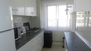 A kitchen with white cabinets, a microwave, a kettle, and a window with sheer curtains. - Apartamento Beata Para 4 Personas (Calpe)