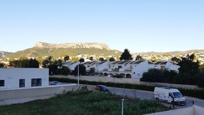 A parking lot with several white cars and a white van. In the background, there are white buildings and a mountain. - Apartamento Beata Para 4 Personas (Calpe)