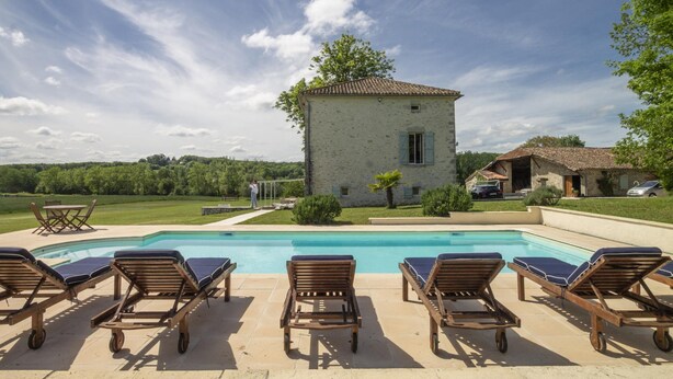 Una piscina con lettini, un edificio in pietra e un paesaggio erboso.