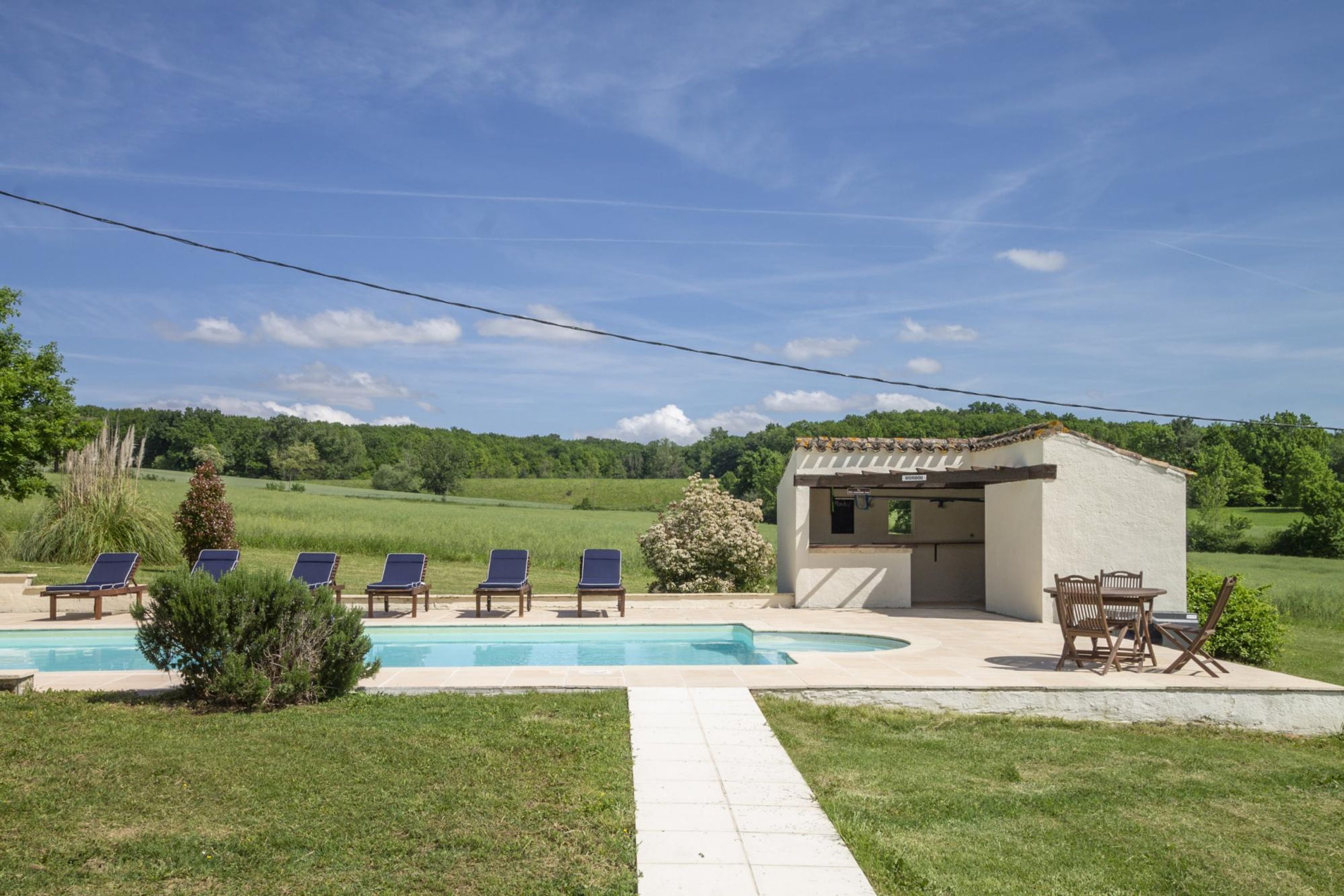 Un área de piscina con sillas de descanso y una pequeña cocina al aire libre.