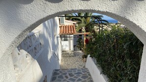 A narrow stone pathway leading to a white-walled building with a tiled roof visible through an archway. - Villa Emilia 4 Personas (Calpe)