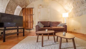 A cozy living room with a television, a brown leather sofa, two wooden side tables, and a white rug. - La Petite Baronne - in the Heart of the Gard (Saint-Hilaire-d'Ozilhan)