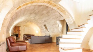 A spacious living area with a stone vaulted ceiling, a leather sofa, a gray couch, and a staircase with wooden steps. - La Petite Baronne - in the Heart of the Gard (Saint-Hilaire-d'Ozilhan)