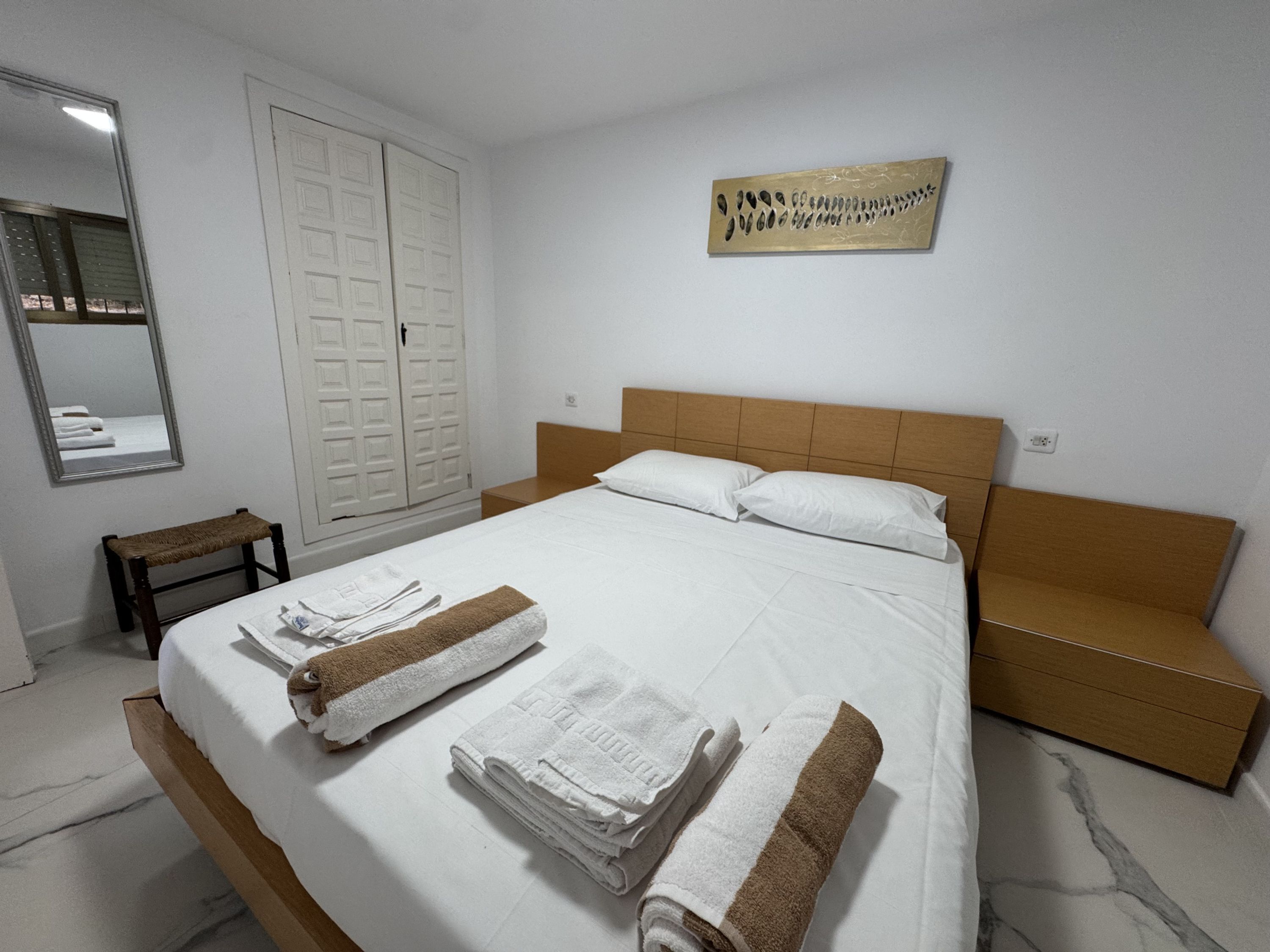 Une chambre d’hôtel comprenant un lit, un banc en bois, une armoire, un miroir et une œuvre d’art murale.