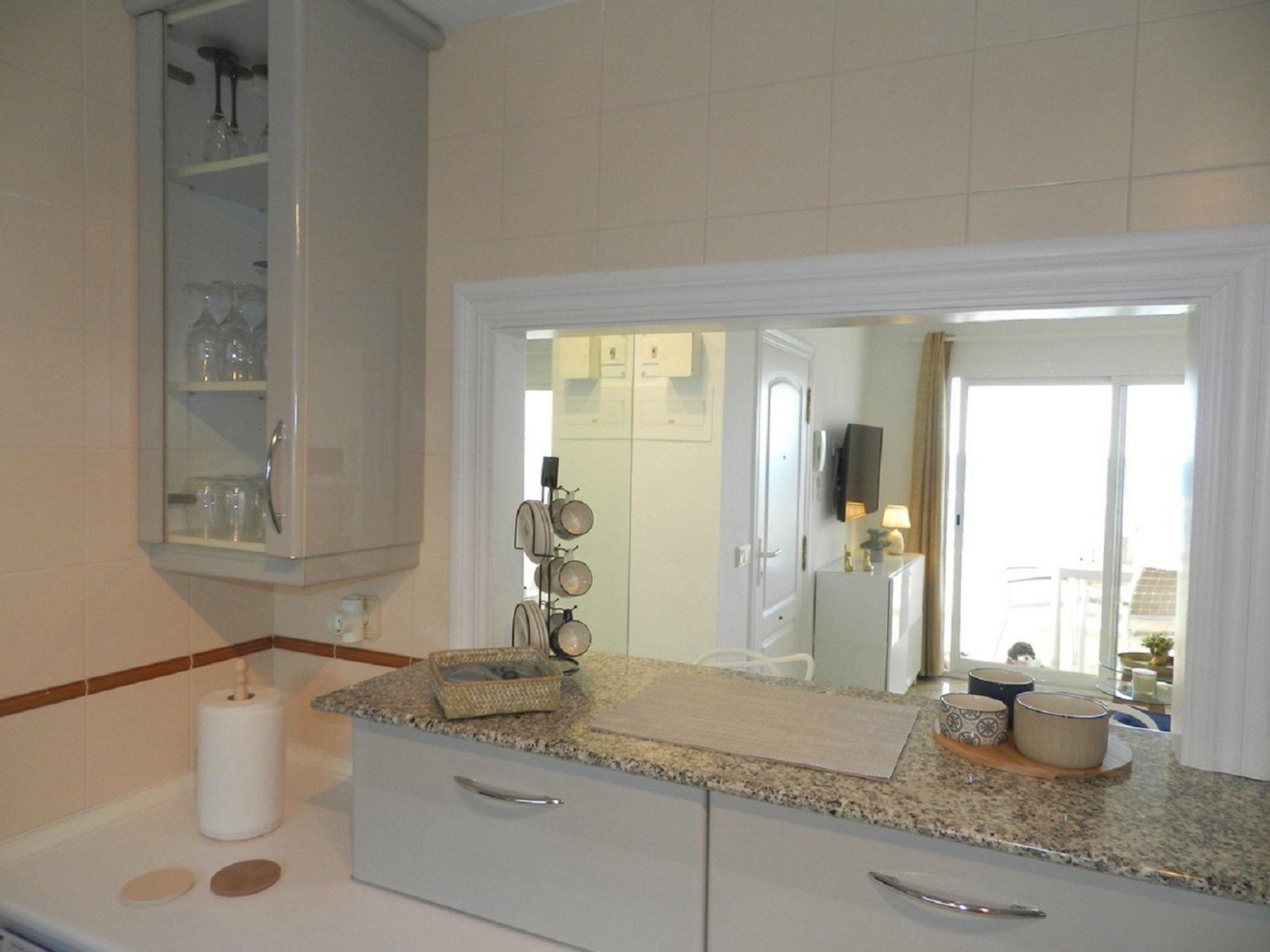 A kitchen with a granite countertop, white cabinets, and a built-in oven. There is a mirror above the countertop and a door leading to another room.