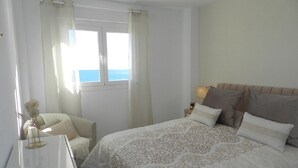 A bedroom with a bed, a bedside table, a chair, and a window with curtains. - Apartamento Mar Timo 4 Personas (Calpe)