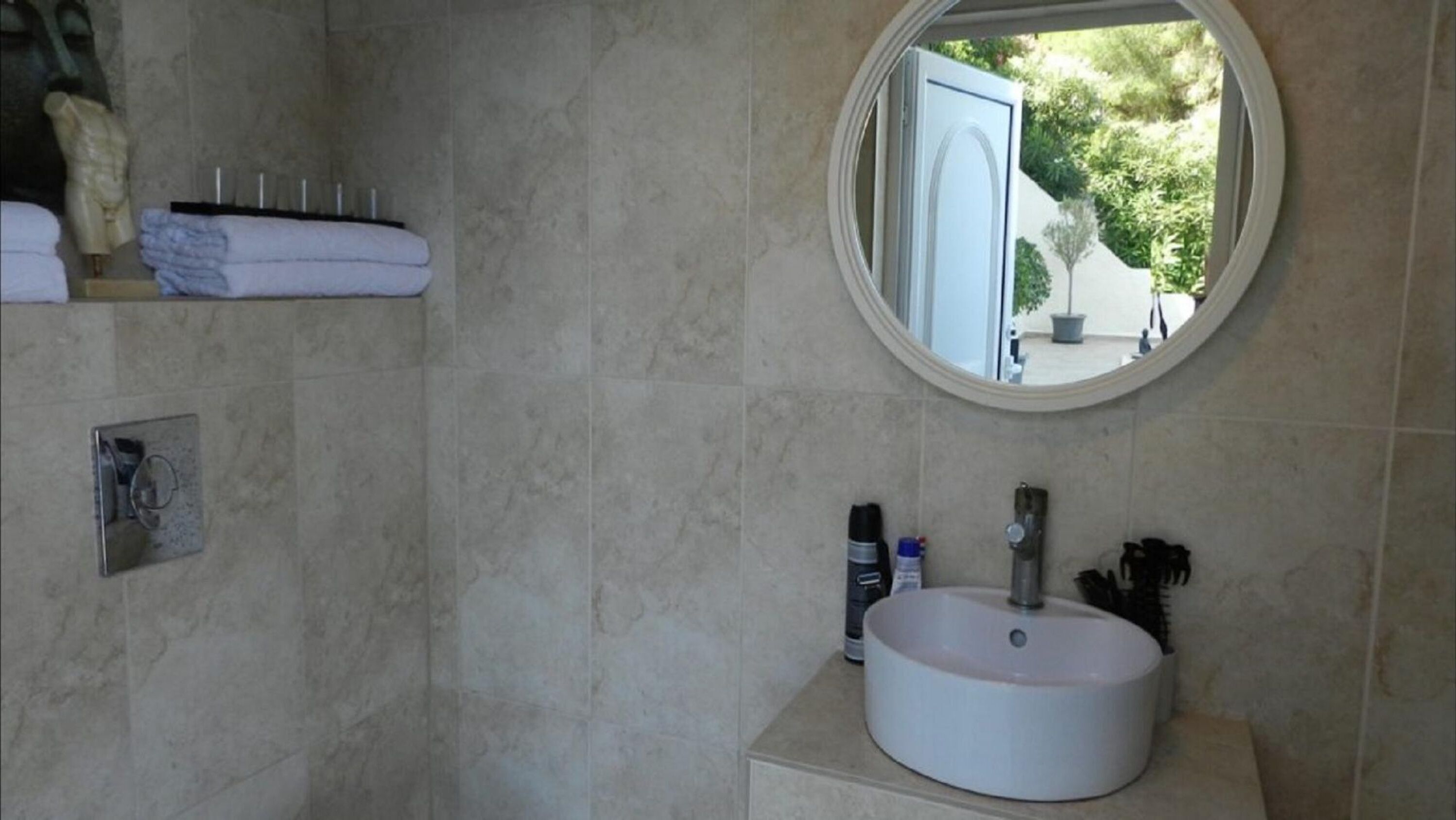 A bathroom with a round mirror, a sink, and a towel rack.