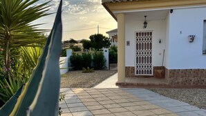 Una casa con un patio empedrado, un portón y un pequeño jardín con una palmera.