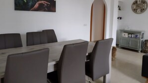 Comedor con una mesa larga y varias sillas, un reloj en la pared y un mueble con objetos encima.