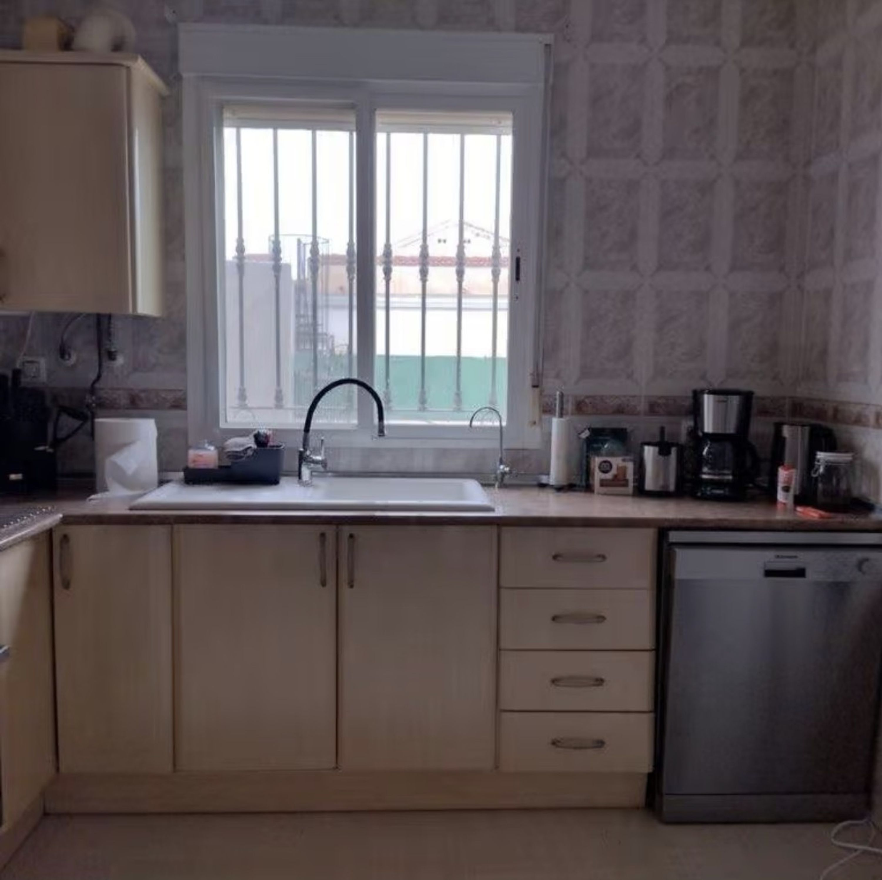 A kitchen with a window, a sink, a coffee maker, and a dishwasher.