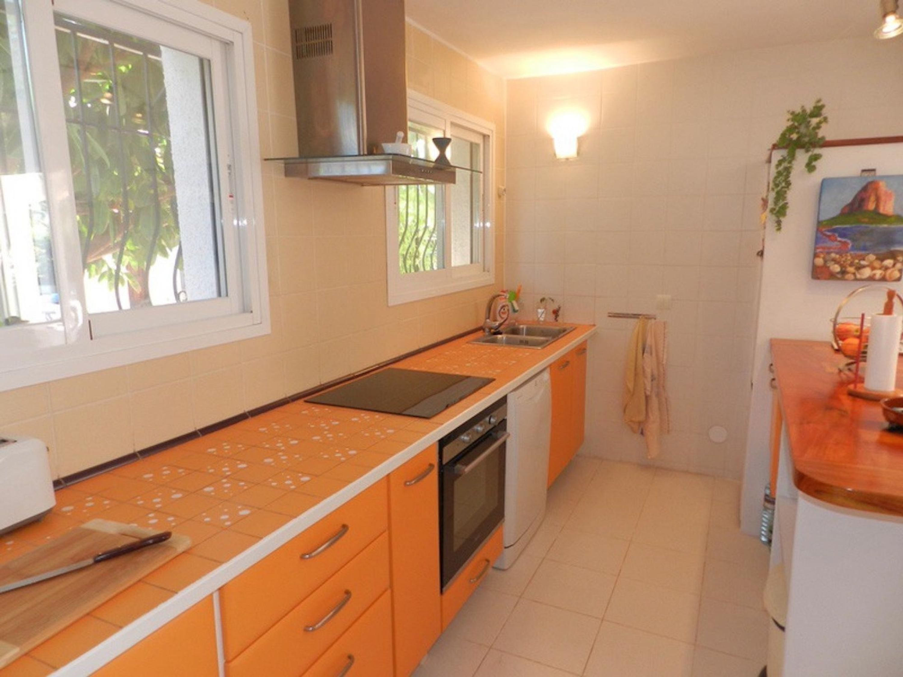 A compact kitchen with a stove, sink, and orange cabinets.