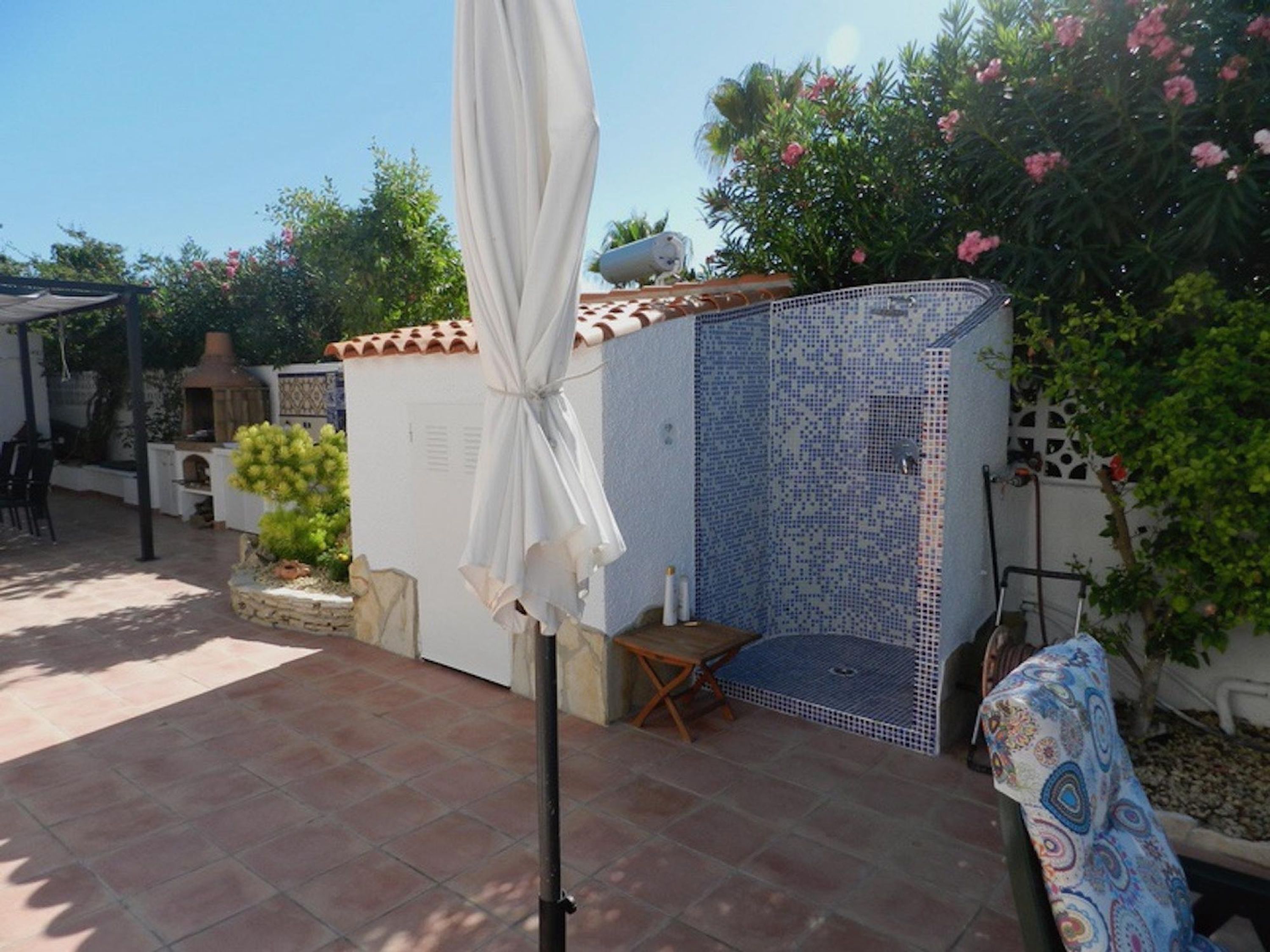 A patio area with a white umbrella, a tiled wall, and a small seating area.