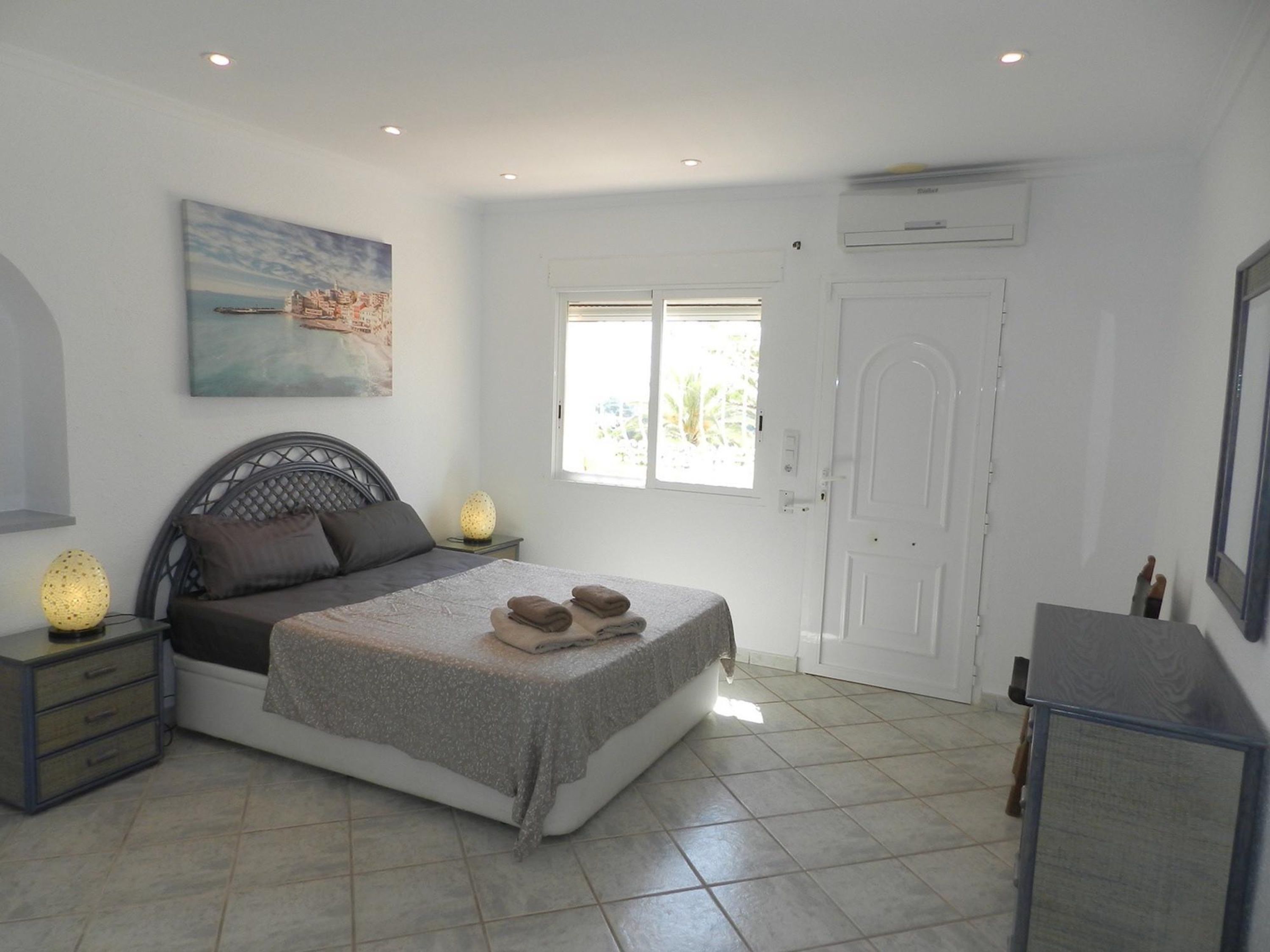 Un dormitorio con cama, lámparas de noche, un cuadro, una ventana y una puerta.