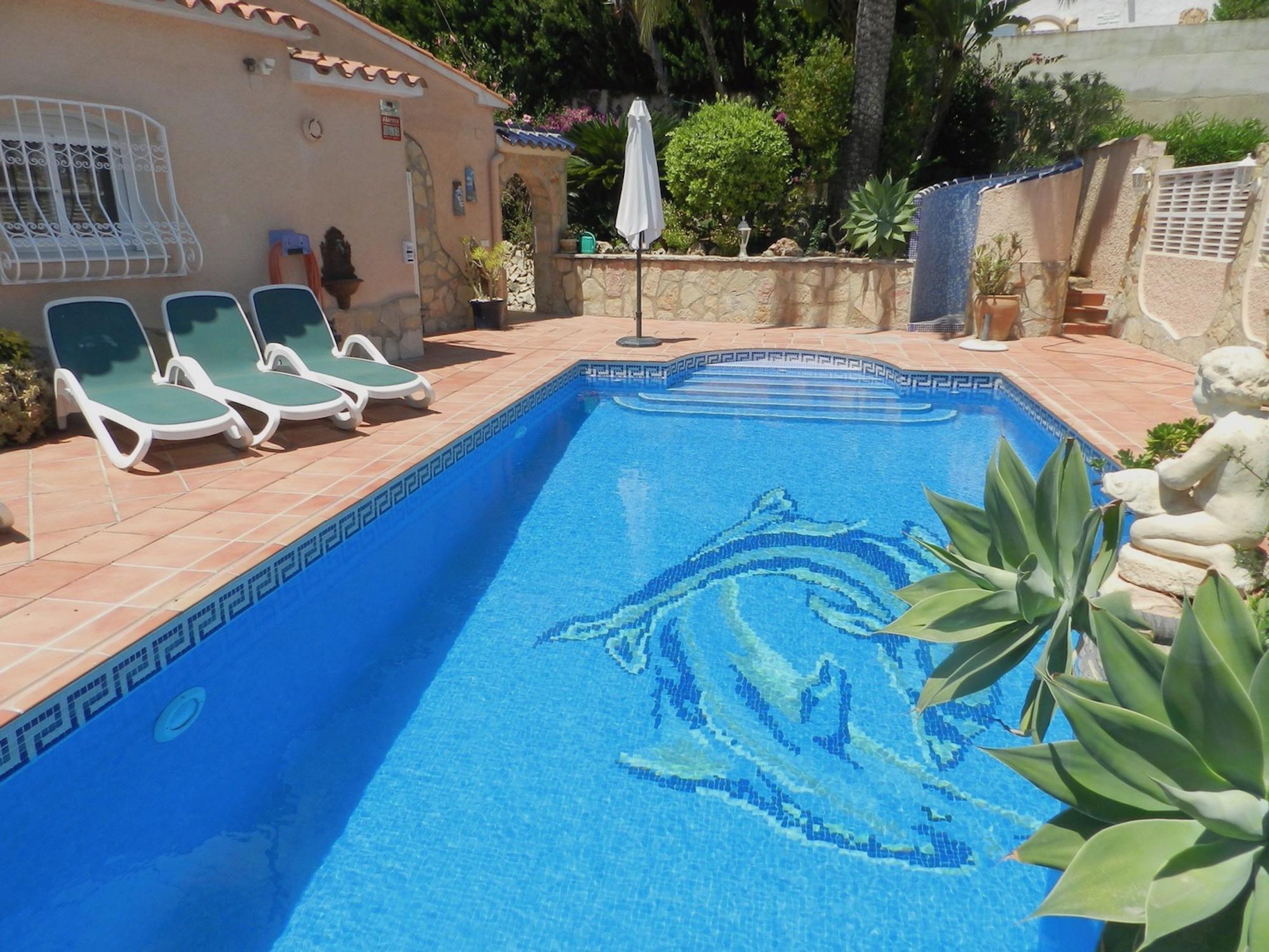A swimming pool with a dolphin mosaic, lounge chairs, and a stone wall.