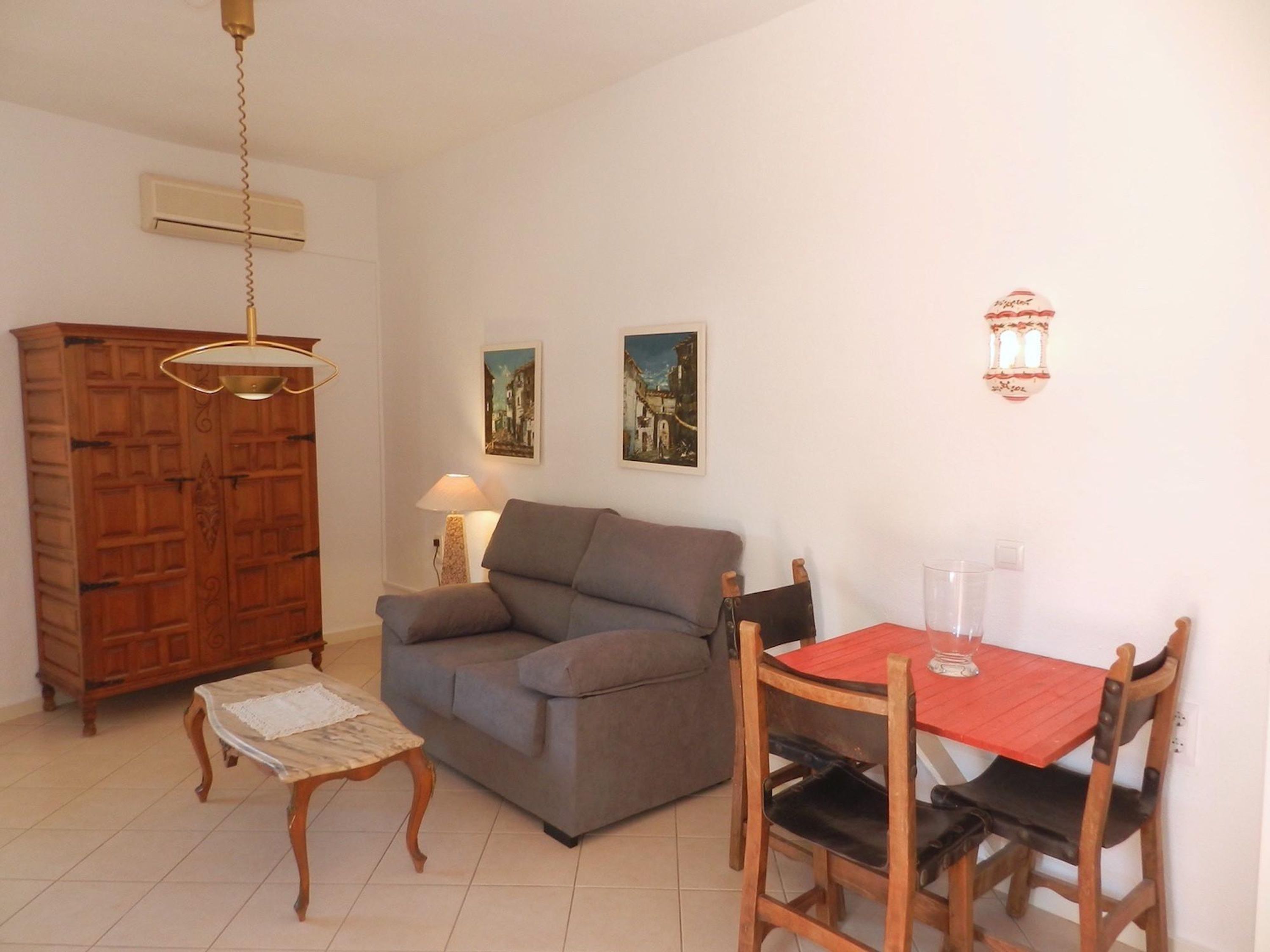 A living room with a sofa, a wooden cabinet, a dining table with chairs, and two wall-mounted lamps.
