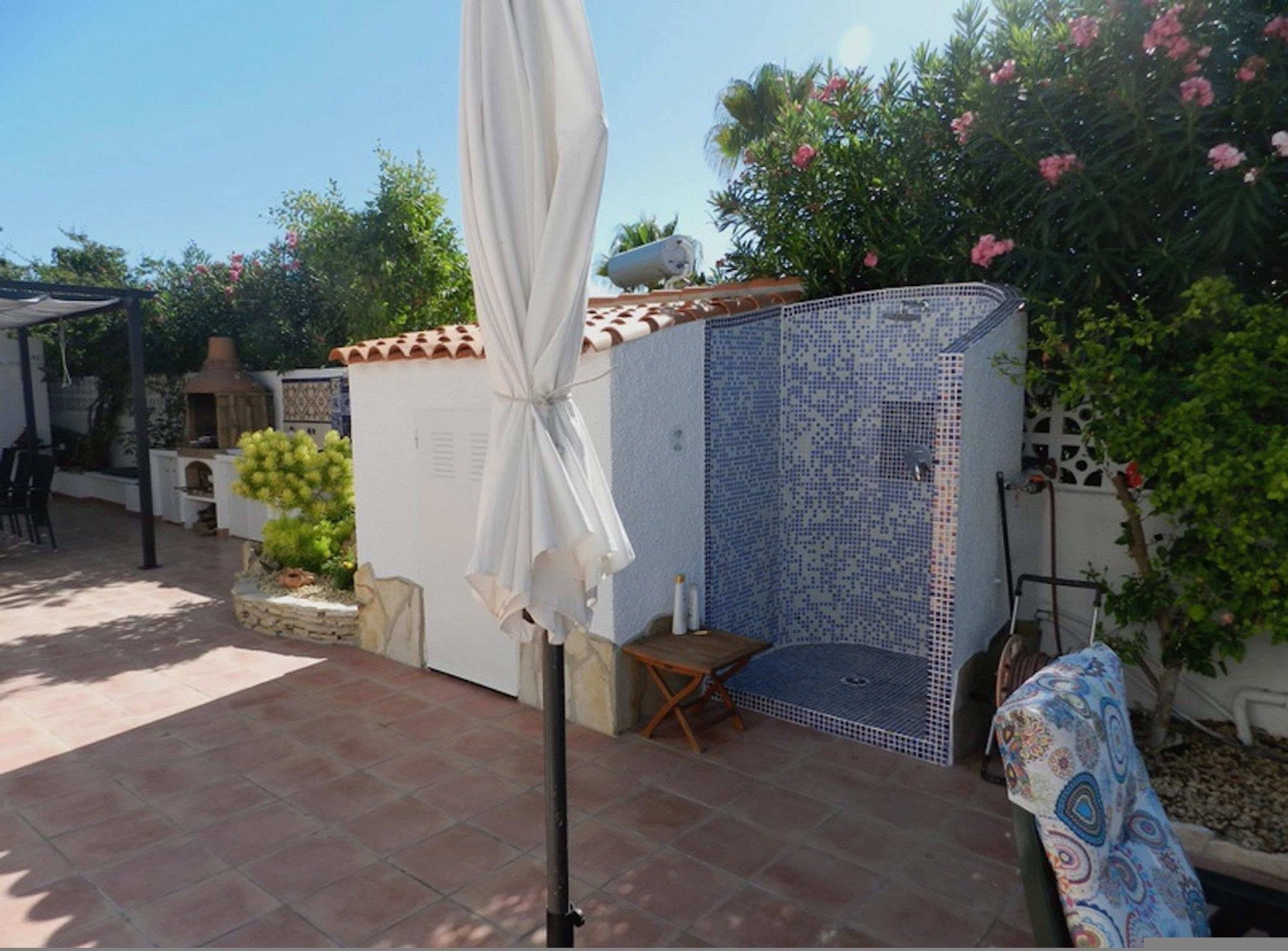 A patio area with a tiled floor, a white umbrella, a small table, and a seating area with a patterned cushion.