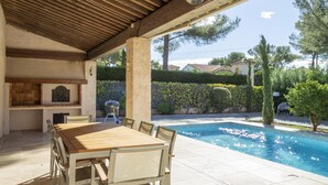 Une terrasse extérieure avec une piscine, une table en bois et un barbecue.