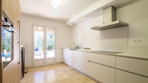Une cuisine moderne avec des armoires blanches, une hotte de cuisinière en acier inoxydable et une vue sur l’extérieur.