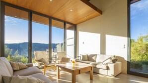 A modern living room with a large window, a wooden ceiling, and a view of the outdoors. - La Maison des Chataigniers (Meyrannes)