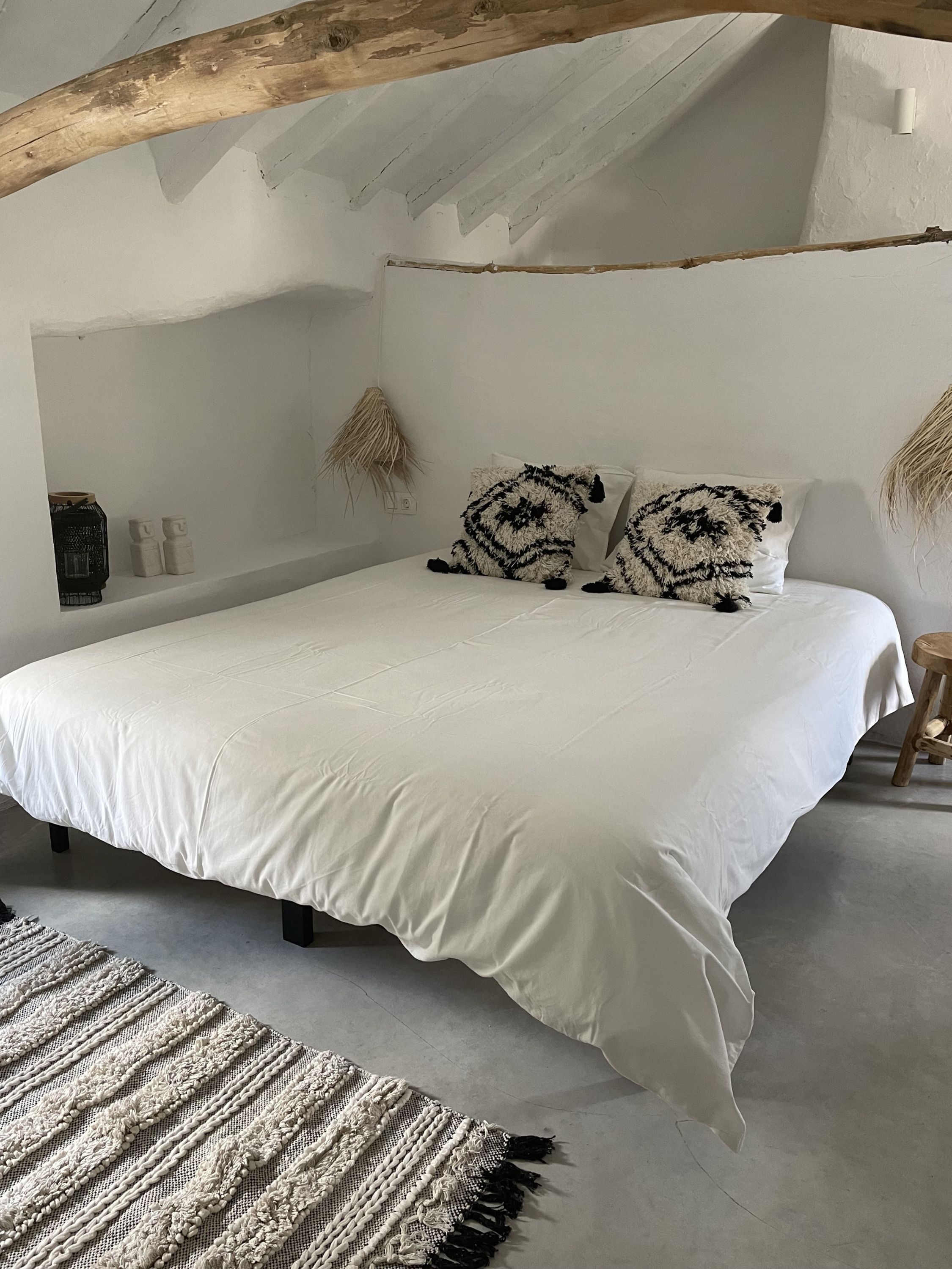 A bedroom with a large bed, a woven rug, and a rustic ceiling beam.