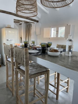 A modern kitchen with a central island, wicker chairs, and a hanging light fixture. - Vista Las Colinas in Izn jar (Iznajar)