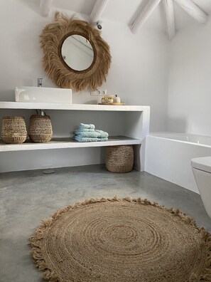 A bathroom with a white sink, mirror, and toilet. There are woven baskets on the shelves and a round woven rug on the floor. - Vista Las Colinas in Izn jar (Iznajar)