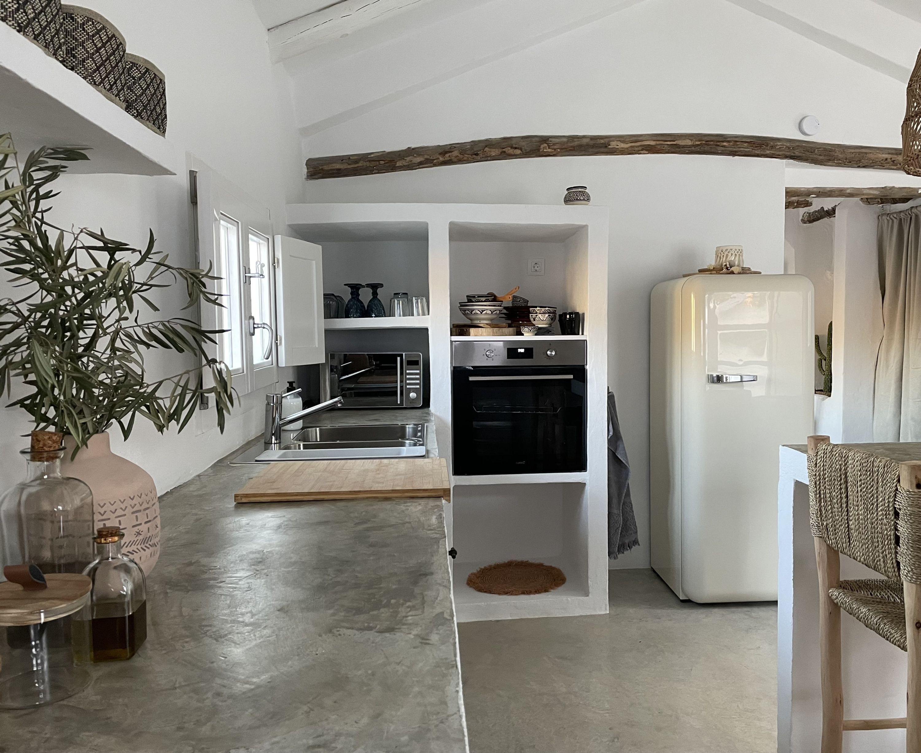 A compact kitchen with a built-in oven, a microwave, and a refrigerator. There is a plant and a bottle on the counter.