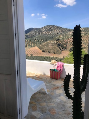 A stone patio with a white plastic chair, a striped bag, and a hat. - Vista Las Colinas in Izn jar (Iznajar)