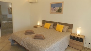 A bedroom with a large bed, two bedside tables, a nightstand, a wall-mounted air conditioner, and a painting on the wall. - Villa Ambiente Para 4 Personas (Calpe)