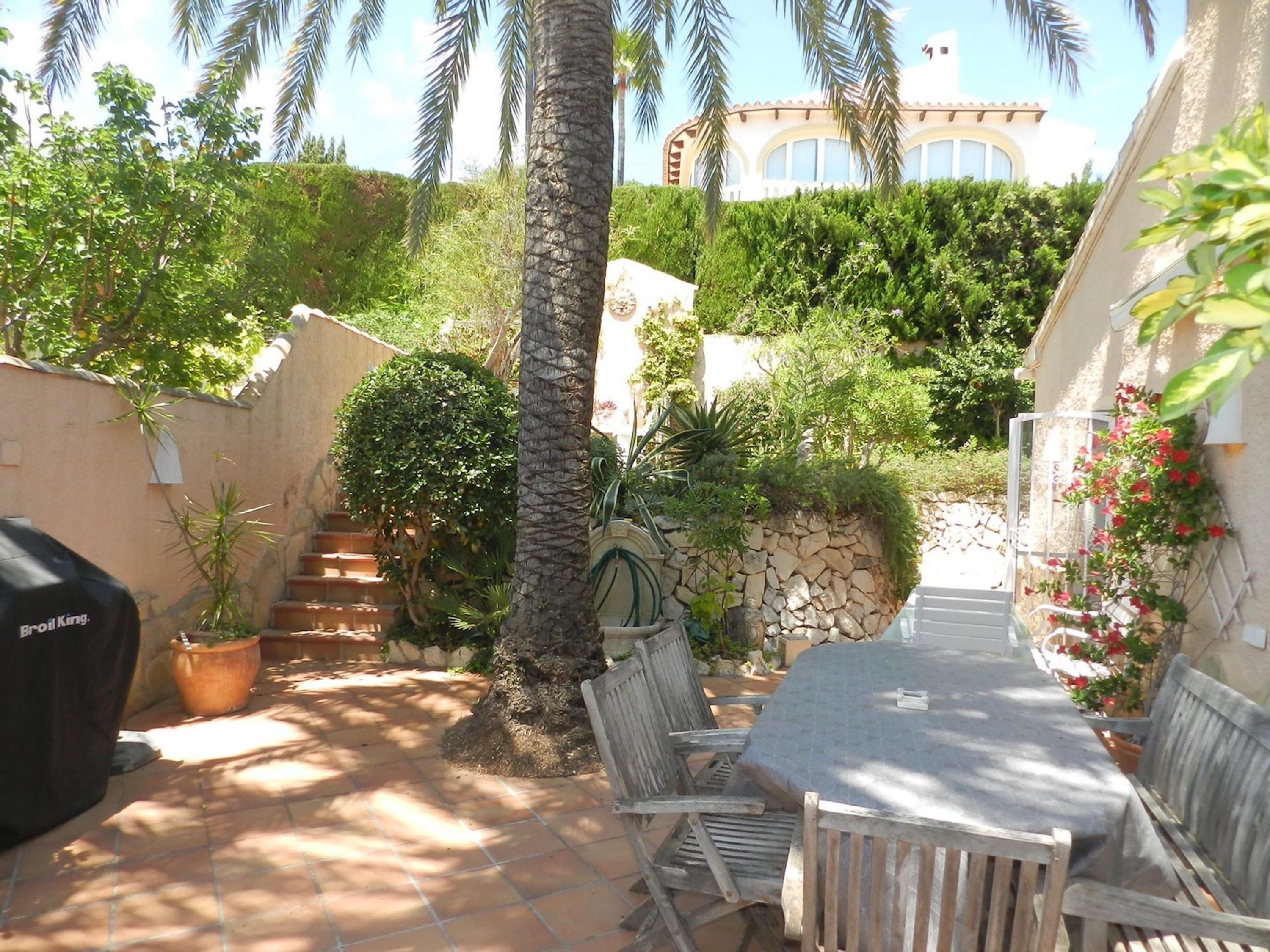 A patio with a table and chairs, surrounded by potted plants and a barbecue grill.