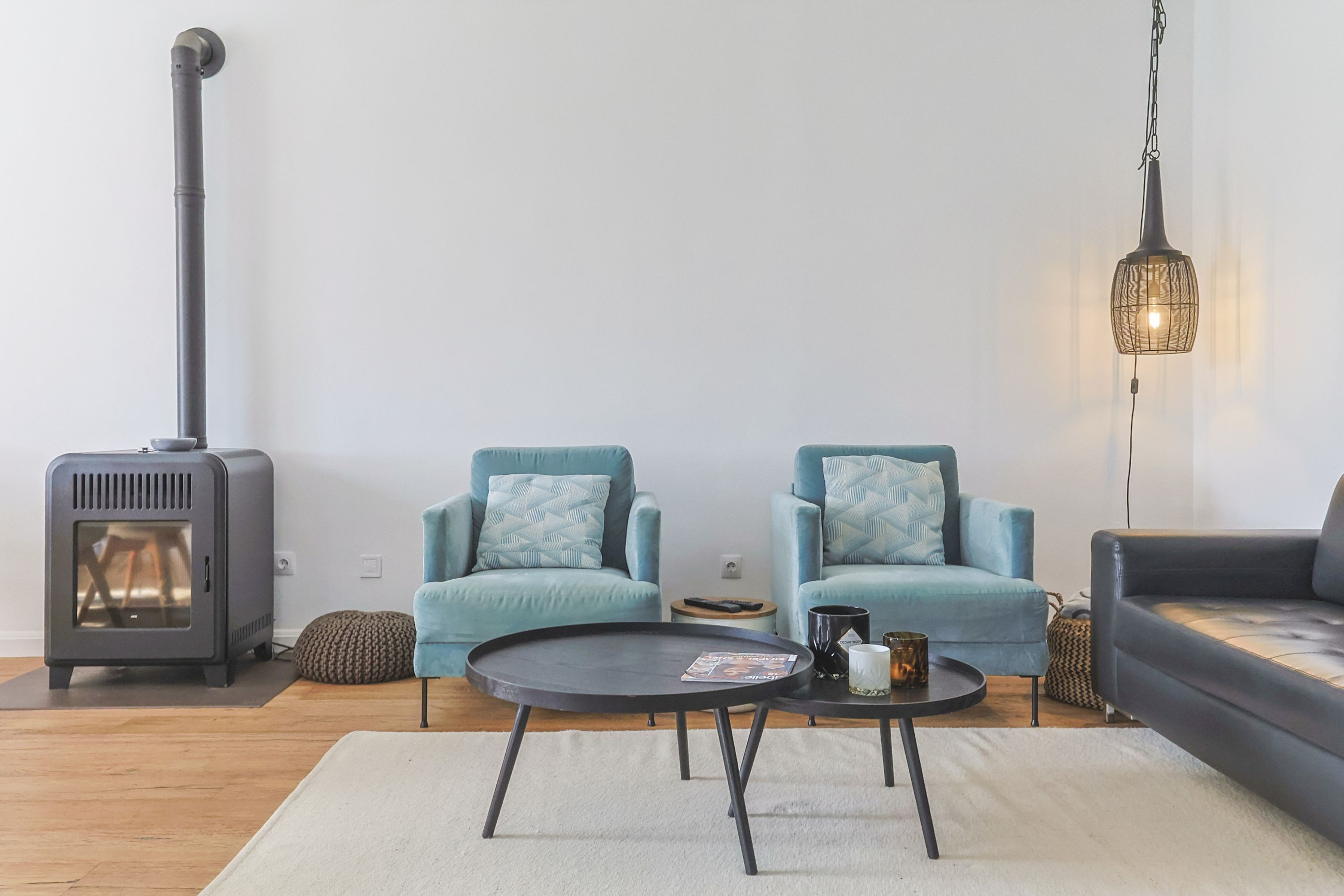 Ein modernes Wohnzimmer mit Kamin, zwei blauen Sesseln, einem schwarzen Couchtisch und einer Pendelleuchte.