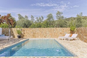 Una piscina rettangolare con una parete in pietra e lettini.