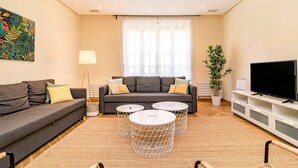 A modern living room with two sofas, a coffee table, a TV, and a large window with sheer curtains.