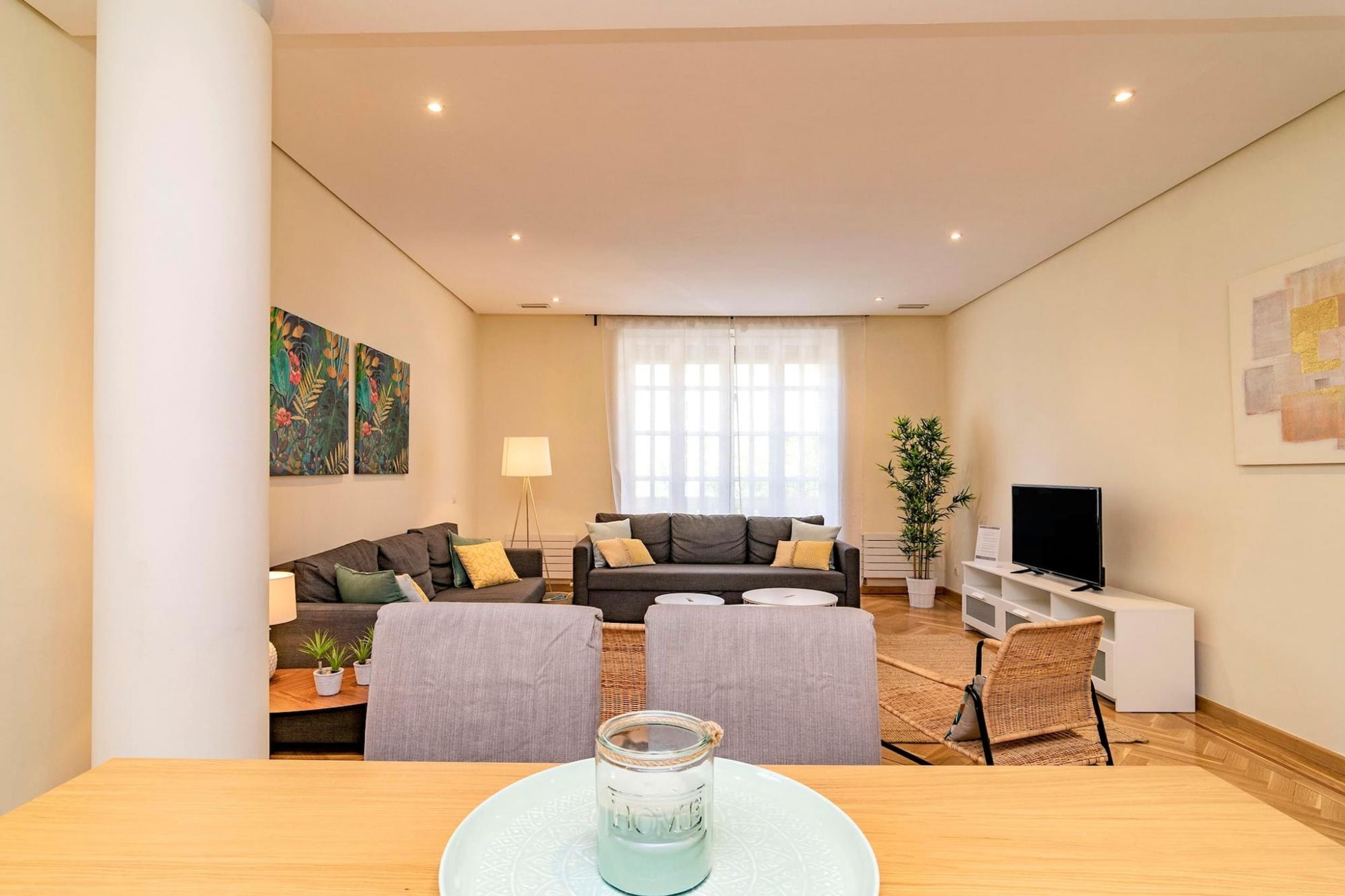 A modern living room with a sofa set, a dining table with chairs, a TV, and a large window with curtains.