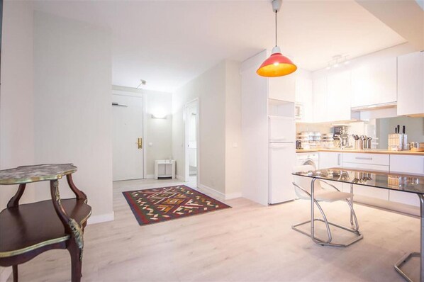 A modern kitchen with white cabinets, a glass dining table, and a colorful rug.