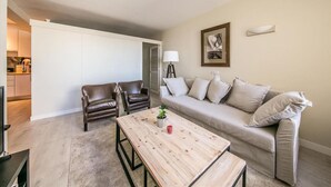 Ein Wohnzimmer mit einer Couch, zwei Sesseln, einem Couchtisch, einer Lampe und einem Gemälde an der Wand.