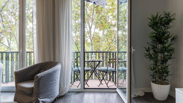 Ein Zimmer mit einer Schiebetür und Glasfront, die auf einen Außenbalkon mit Tisch und Stühlen führt.