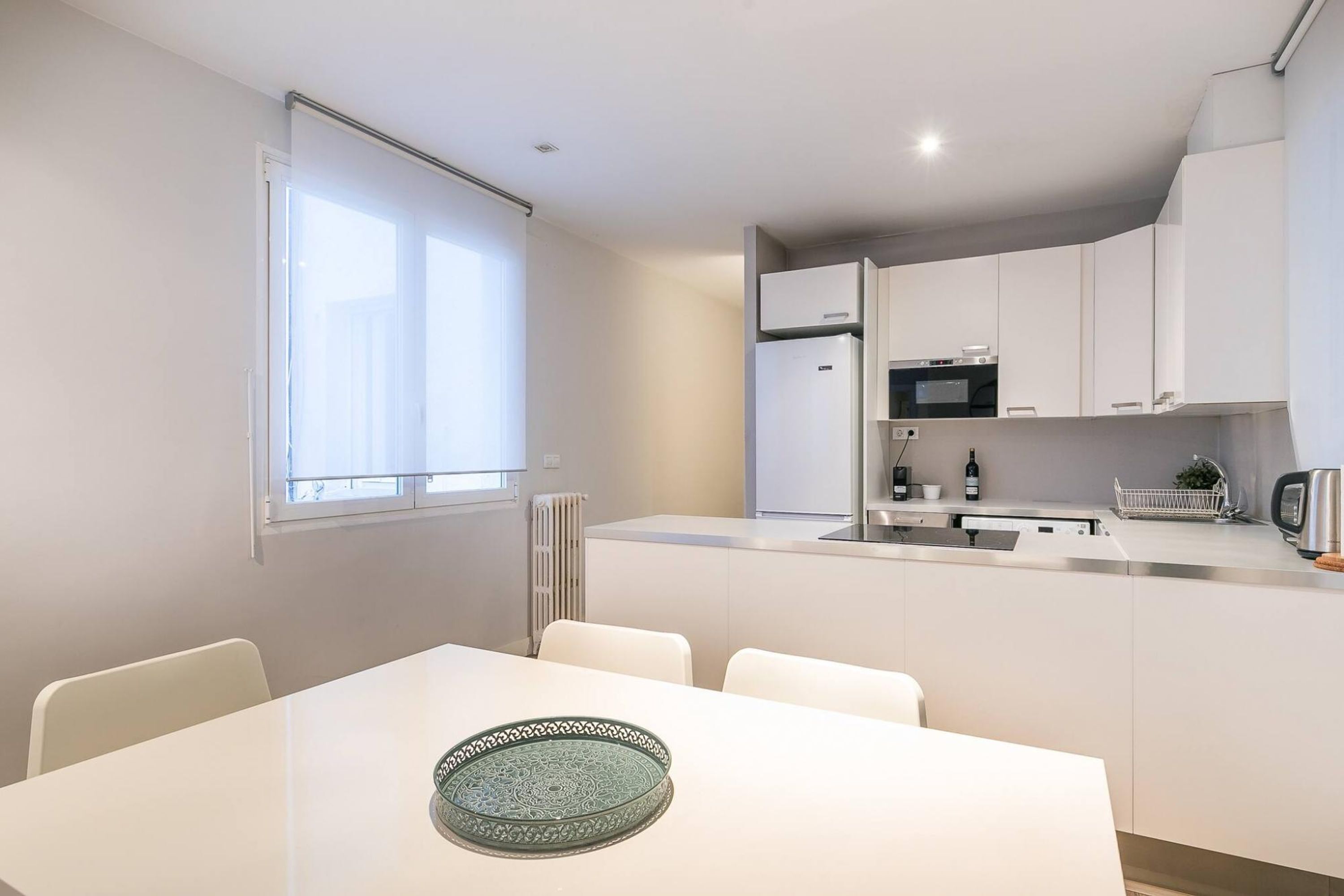 Uma cozinha moderna com armários brancos, forno embutido e micro-ondas. Há uma mesa de jantar com cadeiras e um prato decorativo.