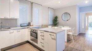 Eine moderne Küche mit weißen Schränken, einer zentralen Kochinsel und einem Essbereich mit rundem Spiegel an der Wand.