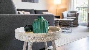 Ein modernes Wohnzimmer mit einem grauen Sofa, einem kleinen runden Tisch mit einer dekorativen Vase und einer Lampe im Hintergrund.