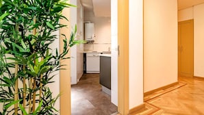 A narrow hallway with a bamboo plant on the left, leading to a kitchen area with white appliances and a dishwasher. - Ddl20 I 2A in Madrid (Madrid)